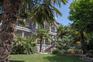 Un edificio de varios pisos con balcones, rodeado de palmeras y un jardín cuidado.