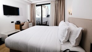 Ein Hotelzimmer mit einem großen Bett, einem Schreibtisch mit Stuhl, einem Flachbildfernseher und einem Balkon mit Vorhängen.