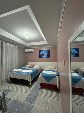Una habitación de hotel con dos camas, una lámpara en el techo, aire acondicionado y un espejo.