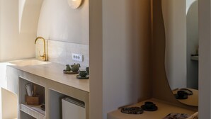 A modern bathroom with a freestanding sink, a gold faucet, and a mirror with a light above it. - Arch Suites (Santorini)