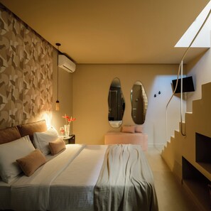 A hotel room with a bed, bedside table, wall-mounted air conditioning unit, two mirrors, a TV, and a staircase. - Arch Suites (Santorini)