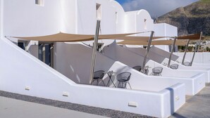 A row of white buildings with outdoor seating and a mountain in the background. - Arch Suites (Santorini)