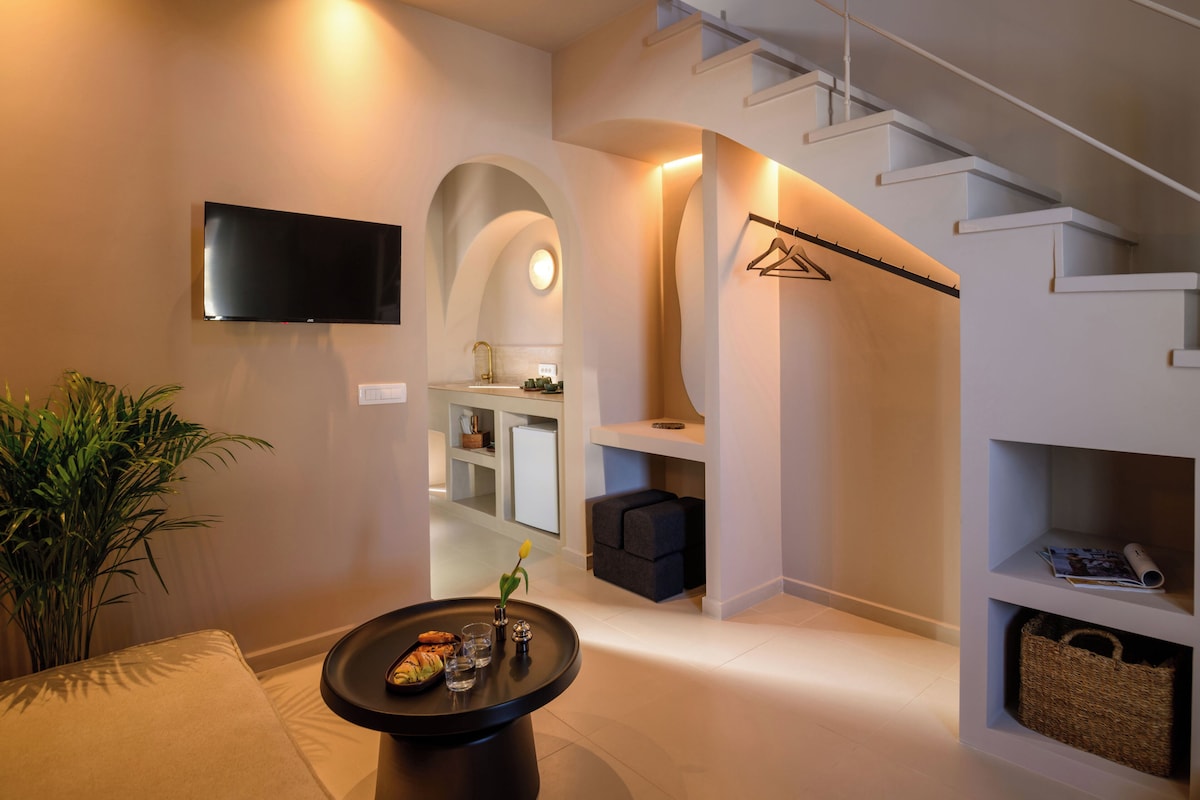 A modern interior with a flat-screen TV, a round table with snacks, a staircase, and a plant.
