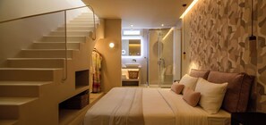 A bedroom with a bed, a staircase, a bathroom with a glass shower, and a patterned wall. - Arch Suites (Santorini)