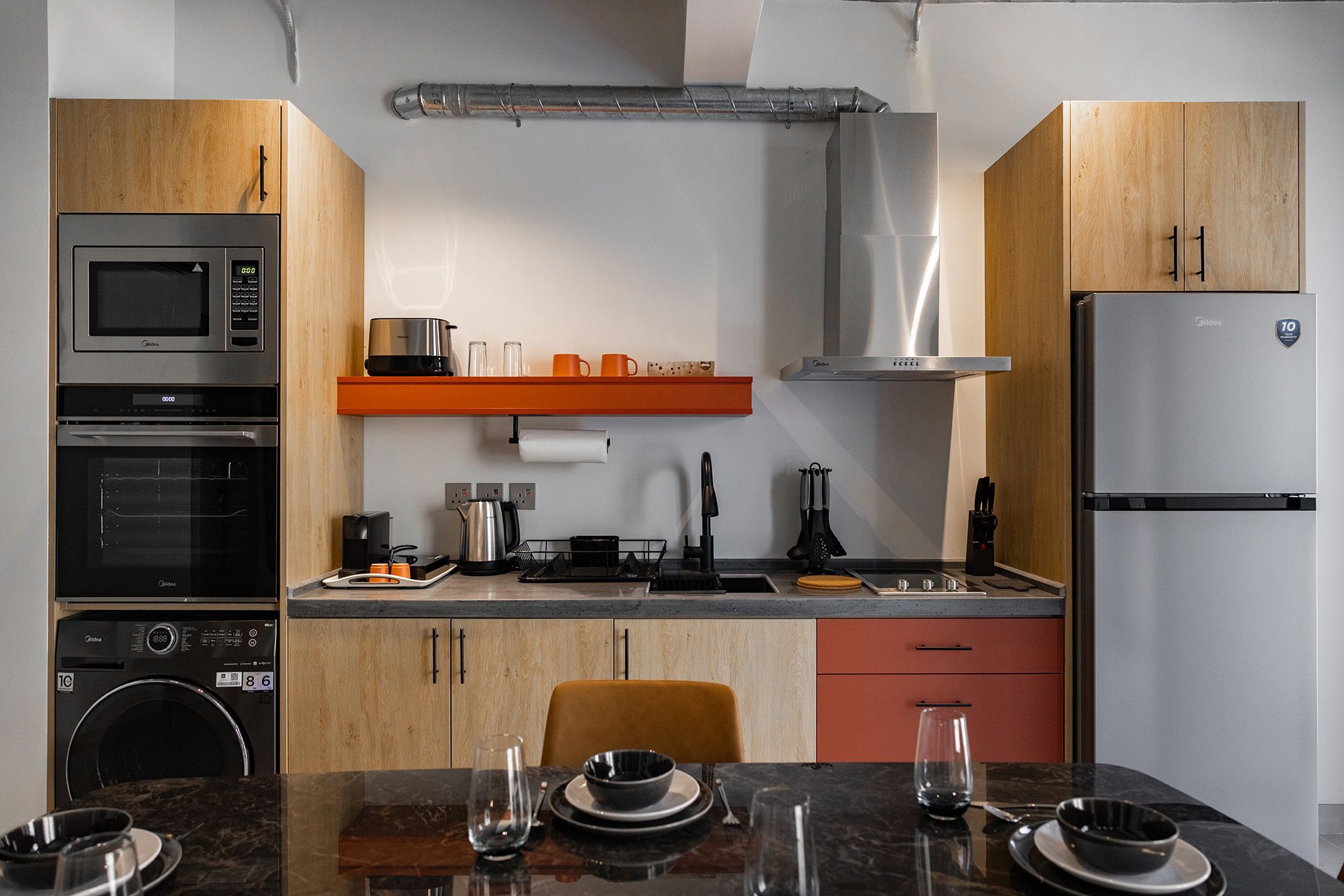 A modern kitchen with built-in appliances, a dining area with a table set for two, and a compact washer and dryer unit.