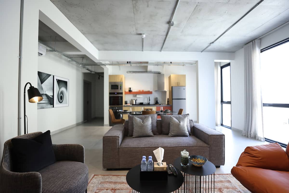 Una sala moderna con un sofá, sillones, una mesa de centro y una cocina al fondo.