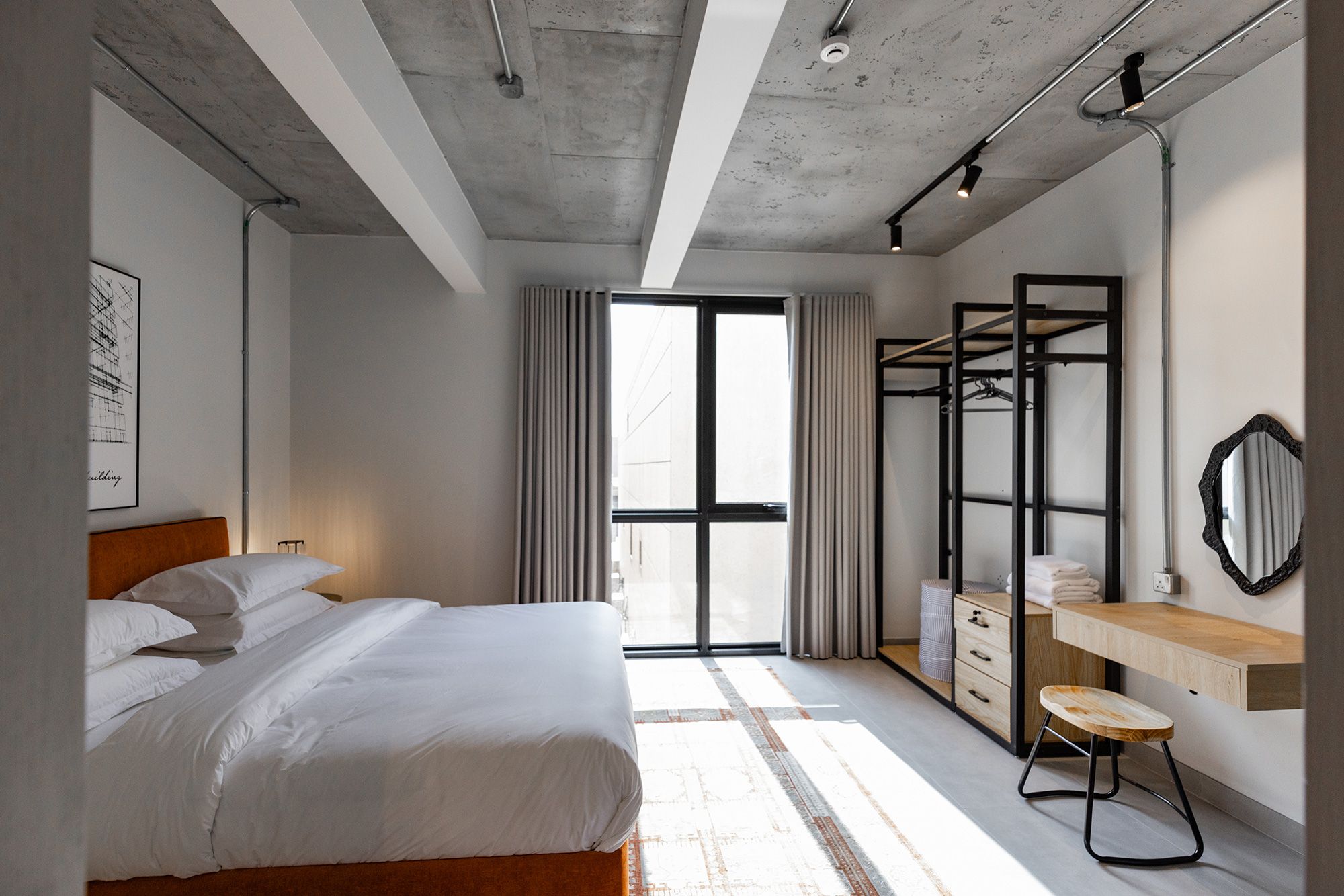 A modern bedroom with a bed, a desk, a wardrobe, and a large window.