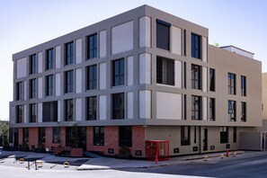 A modern building with a flat facade, multiple windows, and a brick base. - C Living 3 (Madinat Zayed)