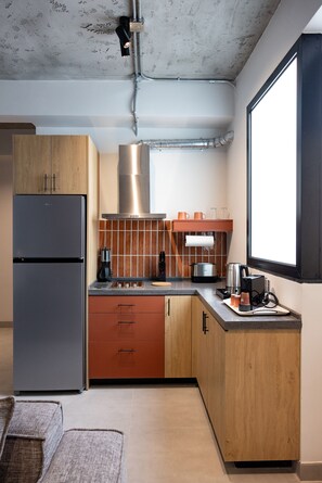 A modern kitchen with a stainless steel refrigerator, wooden cabinets, a gas stove, and a window providing natural light. - C Living 3 (Madinat Zayed)