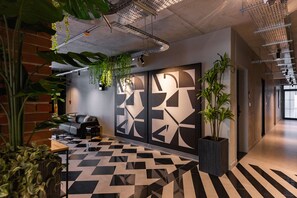 A modern office space with a geometric patterned floor, a brick wall, and hanging plants. - C Living 3 (Madinat Zayed)