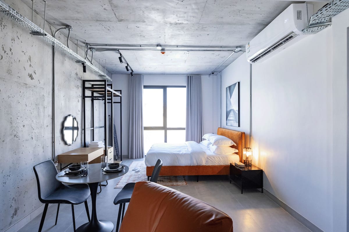 Una habitación de hotel con cama, mesita de noche, lámpara y un comedor con sillas y mesa.
