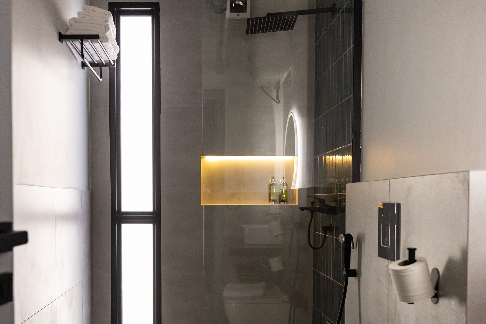 A modern bathroom with a glass shower enclosure, a towel rack, a toilet paper holder, and a shelf with toiletries.