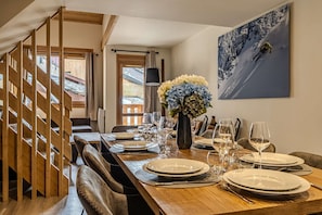 Ein Essbereich mit einem Holztisch, gedeckt für sechs Personen, einer Blumenvase und einem Wandbild zum Thema Skifahren.
