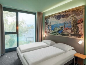 Ein Hotelzimmer mit Bett, Nachttisch, einem Fenster mit Vorhängen und Wandgemälde.