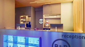 A reception area with a counter, a robot, and a display of wine glasses and bottles. - B&B Hotel Klagenfurt-city (Sankt Veit an der Glan)