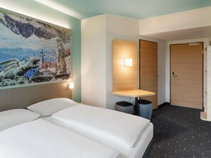 Ein Hotelzimmer mit einem Bett, einem an der Wand befestigten Tisch, einer Tür und einem Mülleimer.
