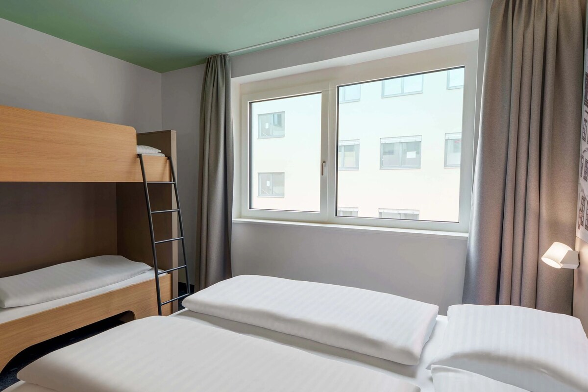 Ein Hotelzimmer mit Etagenbett, einem Fenster mit Vorhängen und Blick auf Gebäude.