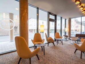Eine moderne Hotelhalle mit großen Fenstern, Sitzbereichen und Blick auf die Straße.