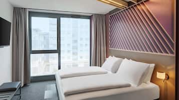 A hotel room with a large bed, a desk, a TV, and a window with a view of buildings.