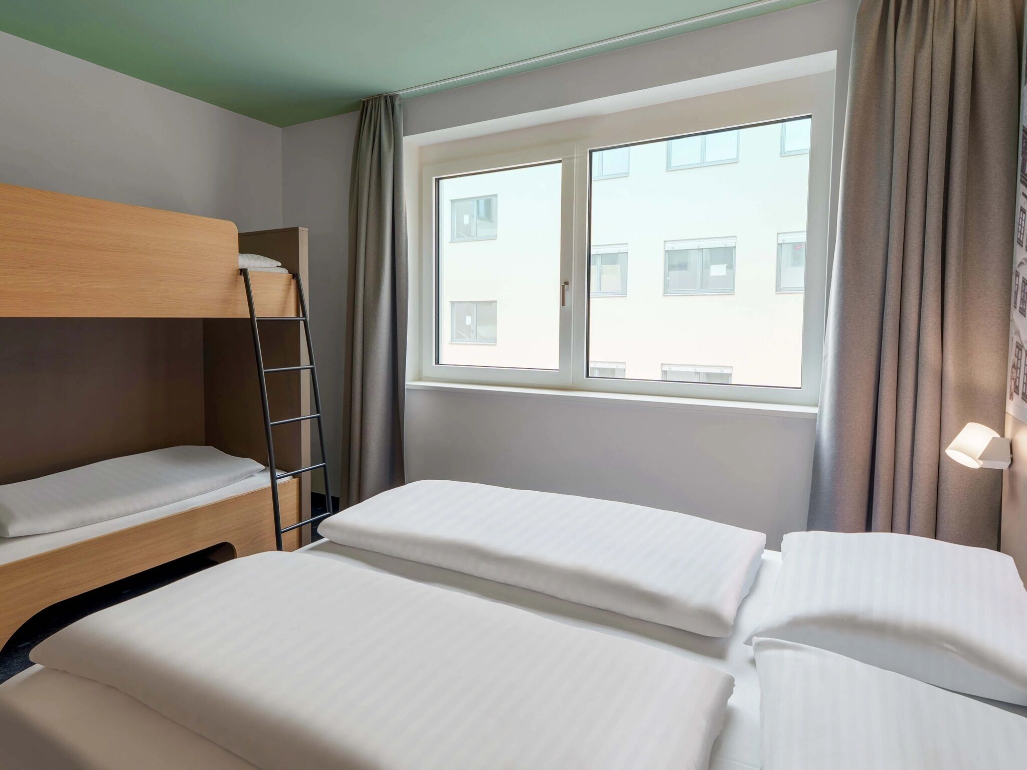 A hotel room with a bunk bed, a window with curtains, and a view of buildings outside.