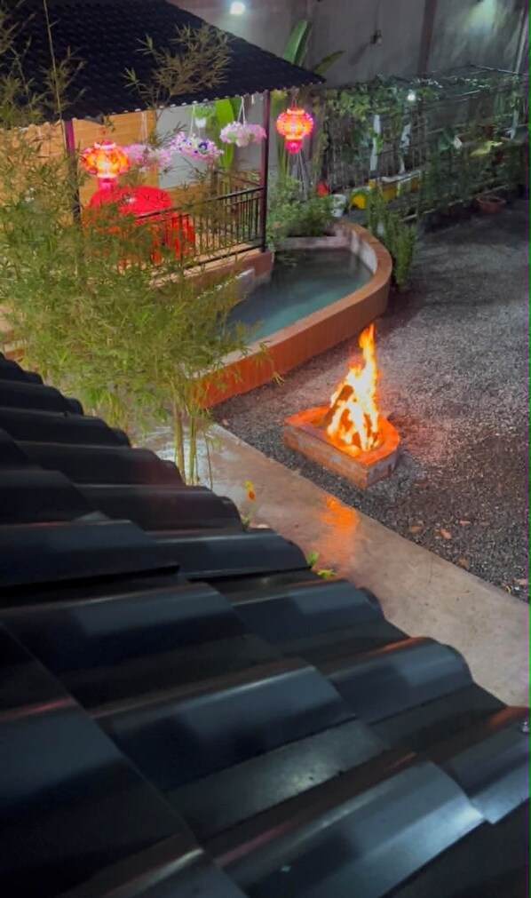 A fire feature in a courtyard with a curved pathway and a small structure with a tiled roof.
