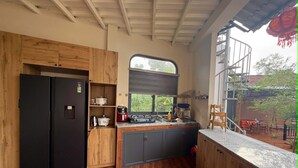 Eine kleine Küche mit Holzausstattung, einem schwarzen Kühlschrank, einem Fenster und Blick ins Freie.