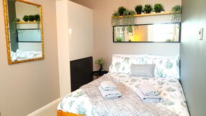 Et soveværelse med seng, sengebord, spejl og en reol med planter.