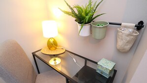 Et værelse med en stol, et bord med en lampe, en potteplante og en skraldespand.