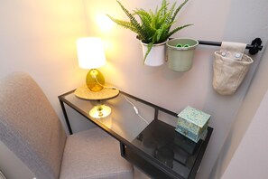 Ein Zimmer mit einem Sessel, einem Tisch mit Lampe, einer Topfpflanze und einem Mülleimer.