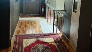 A hallway with a wooden floor, a patterned rug, a chandelier, and a fire extinguisher. - Antique Palace Hotel Baku (Baku)
