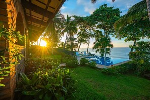 A pool area with lounge chairs, palm trees, and a view of the ocean.