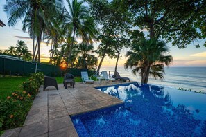 A poolside area with a view of the ocean, palm trees, and lounge chairs.