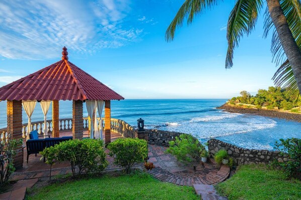 A gazebo with a tiled roof, a stone wall, and a view of the ocean.