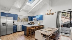 Een moderne keuken met een centraal eiland, blauwe kastjes, een roestvrijstalen koelkast en een groot raam.