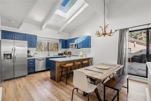Eine moderne Küche mit einer zentralen Kochinsel, blauen Schränken, einem Edelstahlkühlschrank und einem großen Fenster.