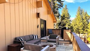 Een houten terras met een bank, stoelen, een vuurkorf en een barbecuehoek.