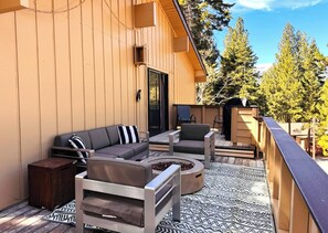 Eine Holzterrasse mit einer Couch, Stühlen, einer Feuerstelle und einem Grillbereich.