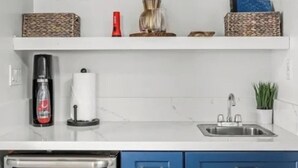 Een keuken met witte planken, een koffieapparaat, een spoelbak en blauwe keukenkastjes.