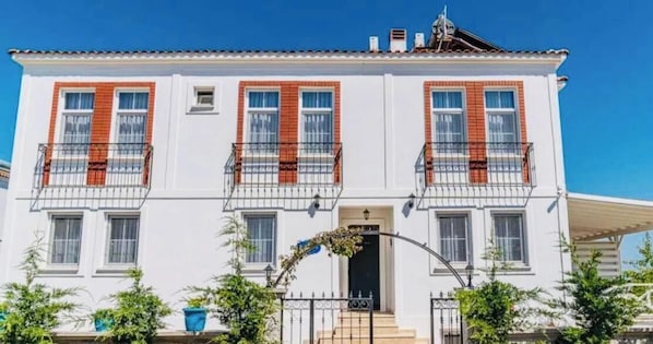 A two-story building with a white facade, red window frames, and a balcony on each floor. - Barbayani Hotel (Bozcaada)