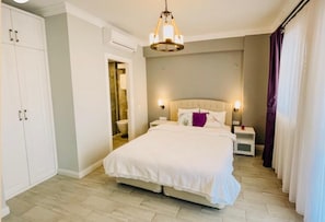 Une chambre à coucher avec un grand lit, une table de chevet, une lampe fixée au mur et une armoire.