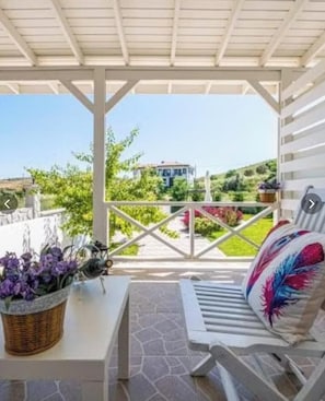 A covered outdoor seating area with a view of a house and greenery. - Barbayani Hotel (Bozcaada)