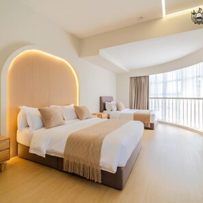 Una habitación de hotel moderna con una cama grande, una cama más pequeña, una mesita de noche, una silla y un amplio ventanal con cortinas.