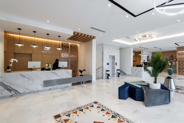A modern hotel lobby with a reception desk, seating area, and a staircase leading to the upper floors.