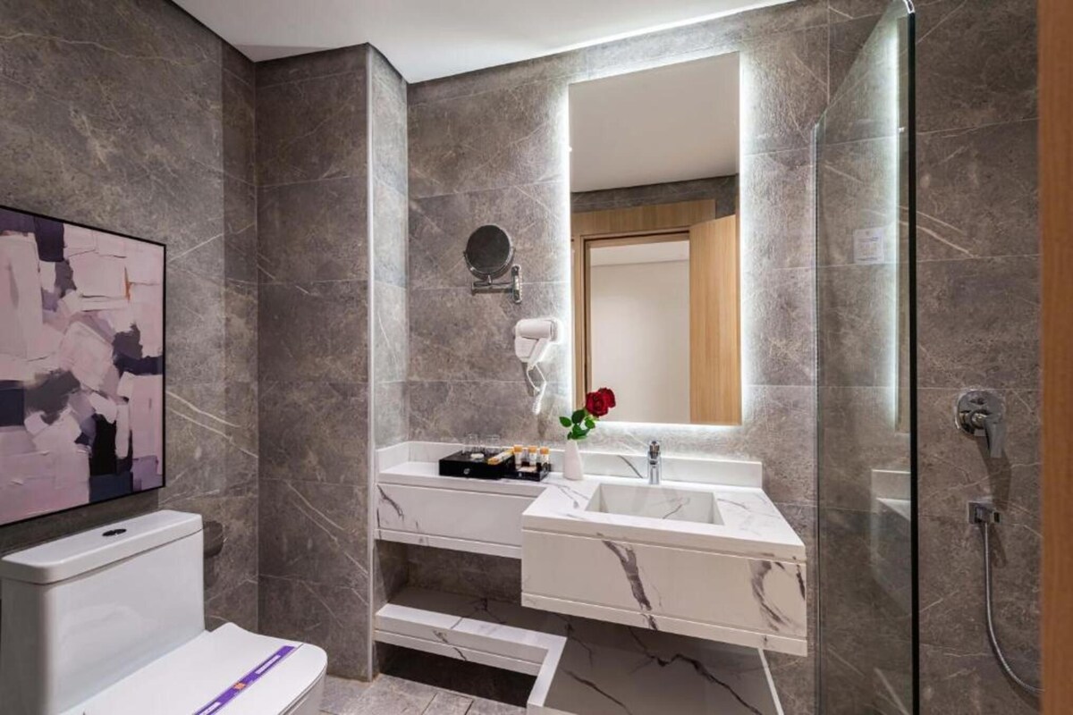 A modern bathroom with a marble sink, a handheld showerhead, and a large mirror.