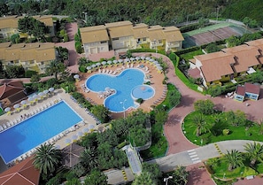 An aerial view of a resort with a central swimming pool, multiple guest rooms, and a tennis court.