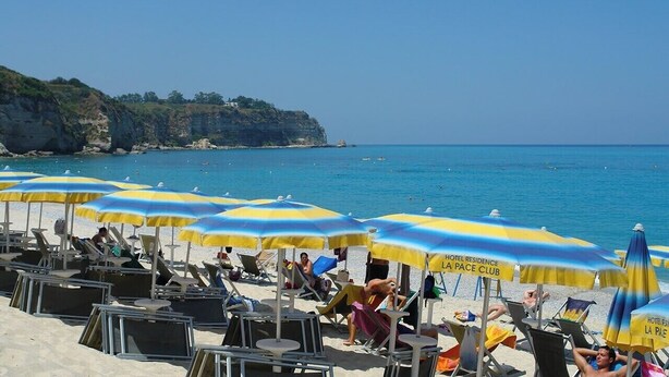 A beach with sun loungers and umbrellas, a clear sky, and a coastline.