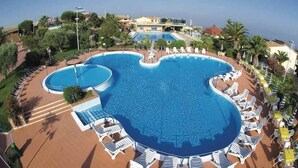 A large swimming pool with a unique shape, surrounded by lounge chairs and umbrellas.