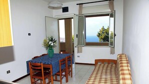 A compact room with a dining table, chairs, a sofa, and a window with a view.