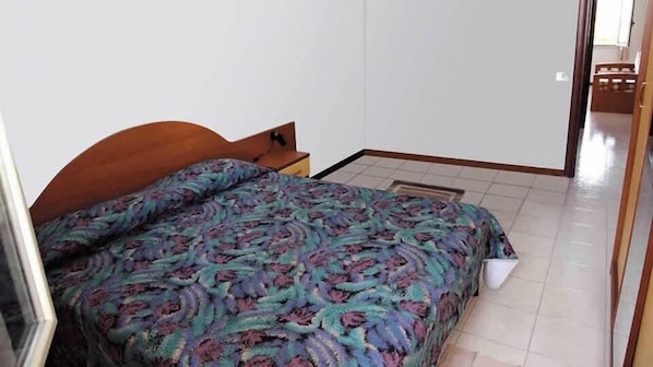 A bedroom with a bed, a wooden headboard, and a white wall.