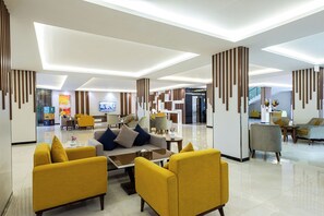 Un moderno vestíbulo de hotel con una zona de estar central, un mostrador de recepción y una escalera que conduce a otras plantas.